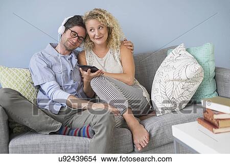 Picture - Couple sitting on sofa listening to music. Fotosearch