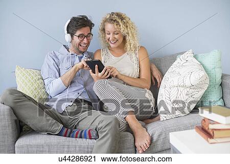 Couple sitting on sofa listening to music View Large Photo Image Stock Image - Couple sitting on sofa listening to music. Fotosearch