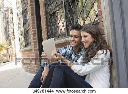 Couple using tablet on sidewalk View Large Photo Image Picture - Couple using tablet on sidewalk. Fotosearch