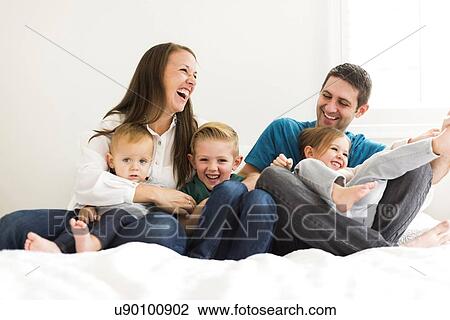 Stock Image - "Family with three children (2-3, 4-5) laughing on bed". Fotosearch