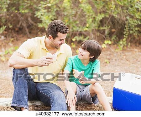 Stock Photo - Father and son (12-13) eating sandwiches in forest. Fotosearch