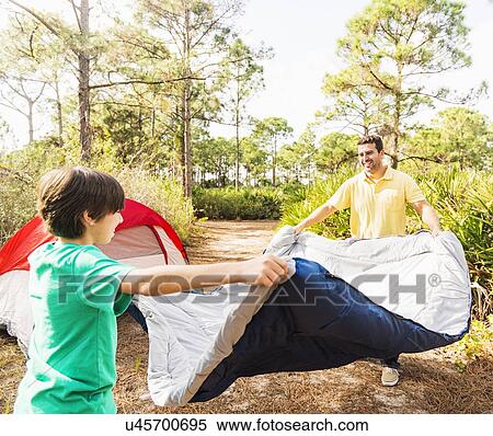 Stock Photography - Father and son (12-13) preparing sleeping bag for camping. Fotosearch