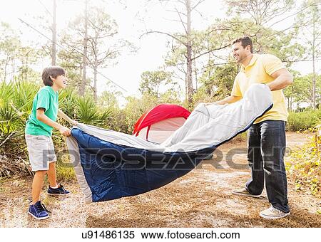 Stock Photography - Father and son (12-13) preparing sleeping bag for camping. Fotosearch