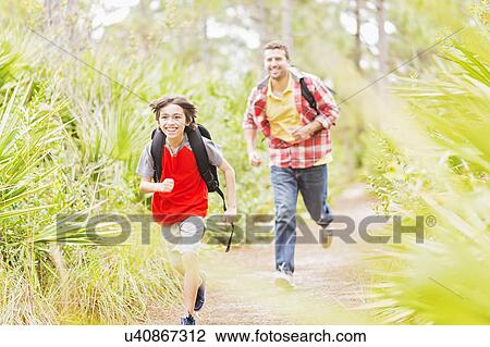 Stock Image - Father and son (12-13) running in forest. Fotosearch