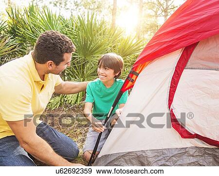 Stock Photo - Father and son (12-13) setting up tent. Fotosearch