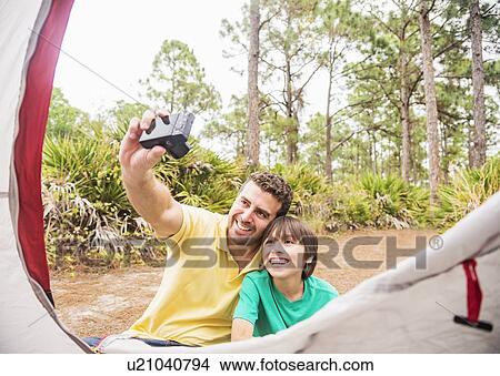 Picture - Father and son (12-13) taking selfie in front of tent. Fotosearch