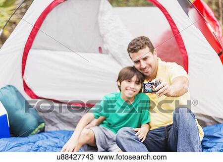 Stock Image - Father and son (12-13) taking selfie in front of tent. Fotosearch