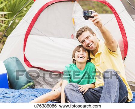 Stock Photograph - Father and son (12-13) taking selfie in front of tent. Fotosearch