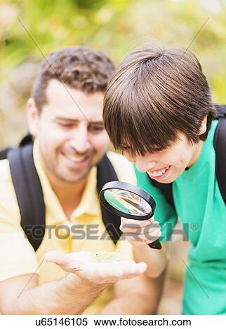Stock Photography - Father and son (12-13) watching insect with magnifying glass. Fotosearch