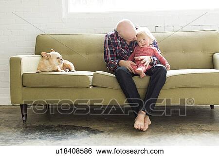 Stock Photograph - Father sitting on sofa embracing baby son (2-3). Fotosearch