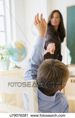 "Female teacher standing beside blackboard in classroom, schoolboy (6-7) with hand raised" View Large Photo Image Stock Image - "Female teacher standing beside blackboard in classroom, schoolboy (6-7) with hand raised". Fotosearch