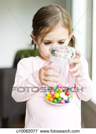 Stock Photo - Girl (4-5) holding glass jar with candies. Fotosearch