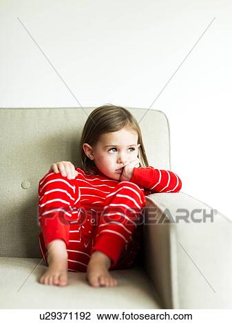 Stock Image - Girl (4-5) in pajamas sitting on sofa. Fotosearch