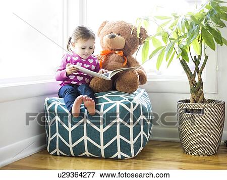 Stock Photo - Girl (4-5) sitting with teddy bear on bean bag. Fotosearch