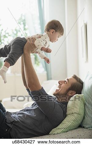 Stock Photo - Happy father playing with little son (2-3 years) on bed. Fotosearch