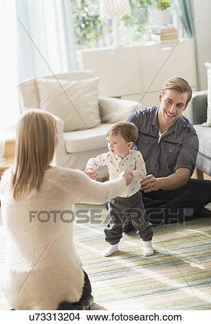 Happy parents helping little son (2-3 years) walking in living room View Large Photo Image Picture - Happy parents helping little son (2-3 years) walking in living room. Fotosearch