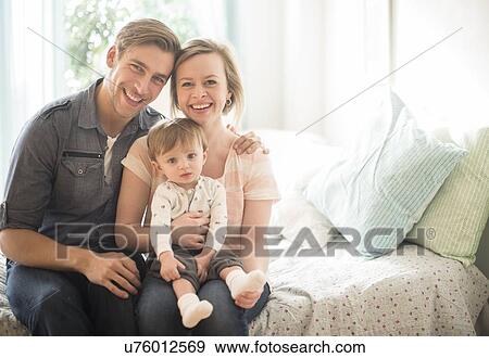 Stock Photo - Happy parents with little son (2-3 years) sitting on bed. Fotosearch