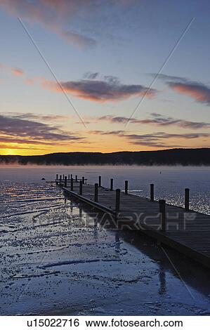 Stock Photograph - "Jetty on frozen lake, hills in background at sunrise". Fotosearch