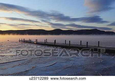 "Jetty on frozen lake with vapor, hills in background at sunrise" View Large Photo Image Stock Photo - "Jetty on frozen lake with vapor, hills in background at sunrise". Fotosearch