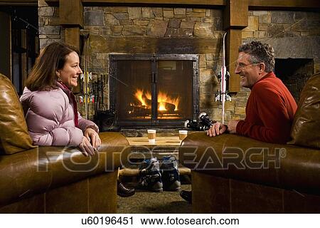 Stock Image - Man and woman chatting in front of fireplace. Fotosearch