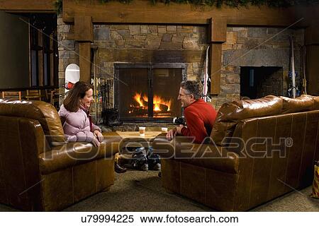 Stock Photography - Man and woman chatting in front of fireplace. Fotosearch