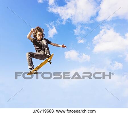 Stock Image - Man jumping on skateboard against sky and clouds. Fotosearch
