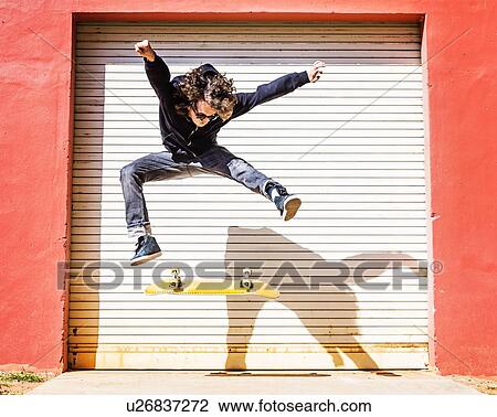 Stock Image - Man jumping on skateboard against closed garage door. Fotosearch