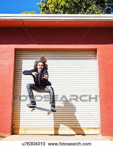 Stock Image - Man jumping on skateboard against closed garage door. Fotosearch