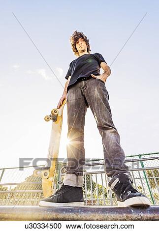 Stock Image - Man leaning on skateboard in skatepark. Fotosearch