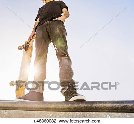 Stock Image - Man leaning on skateboard in skatepark. Fotosearch