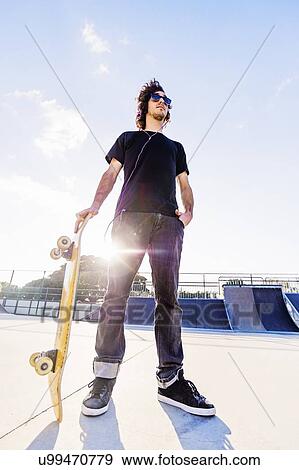 Stock Photo - Man leaning on skateboard in skatepark. Fotosearch