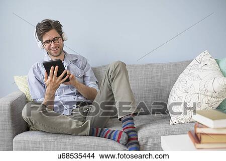 Picture - Man sitting on sofa listening to music. Fotosearch