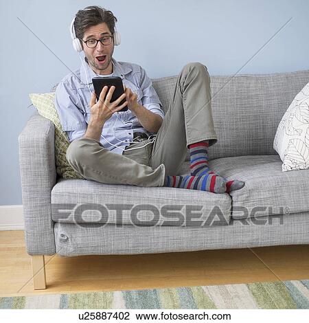 Stock Image - Man sitting on sofa listening to music. Fotosearch