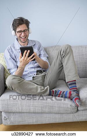 Stock Photo - Man sitting on sofa listening to music. Fotosearch