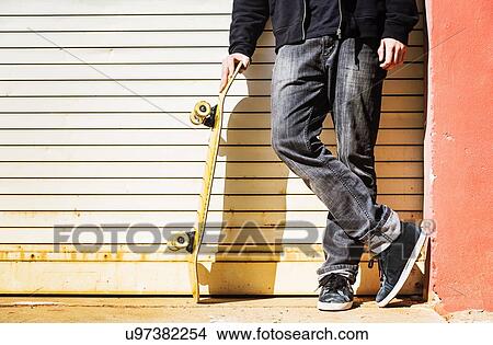 Picture - Man with skateboard leaning on garage door. Fotosearch