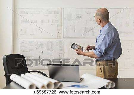 Stock Photograph - Mature architect looking at blueprints in office. Fotosearch
