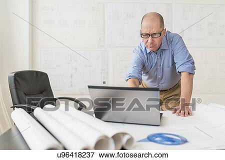 Stock Photo - Mature architect using laptop in office. Fotosearch