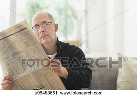 Stock Image - Mature man reading newspaper on sofa . Fotosearch