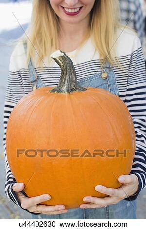 Stock Image - Mid-section of woman showing pumpkin. Fotosearch