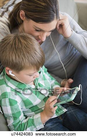 Stock Image - Mother and son (6-7) listening to music. Fotosearch
