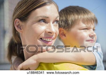 Stock Image - Mother giving her son (6-7) piggyback ride. Fotosearch