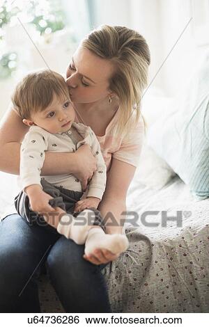 Stock Photograph - Mother kissing little son (2-3 years) on bed. Fotosearch