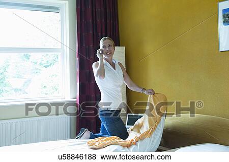 Stock Photo - "Netherlands, Goirle, Mid-adult woman making bed and talking on phone". Fotosearch