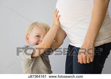 Stock Image - Portrait of boy (2-3) touching his pregnant mom's stomach. Fotosearch