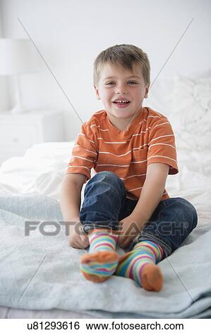 Stock Photograph - Portrait of boy (6-7) sitting on bed. Fotosearch