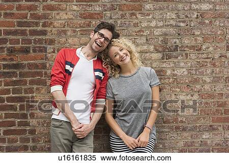 Stock Photography - Portrait of couple standing against brick wall. Fotosearch