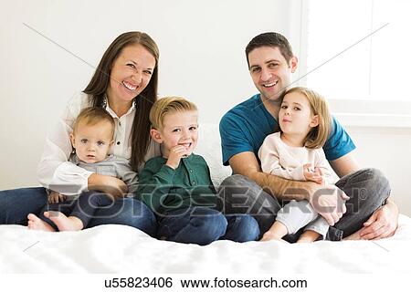 Stock Photograph - "Portrait of family with three children (2-3, 4-5) sitting on bed". Fotosearch