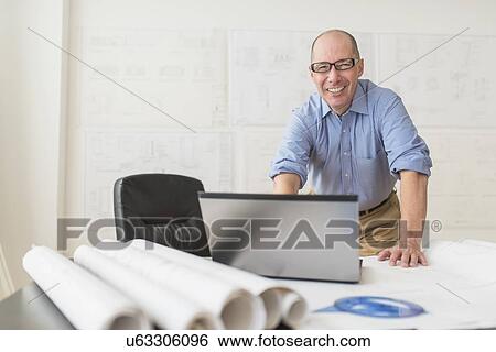 Stock Photograph - Portrait of smiling mature architect using laptop in office. Fotosearch