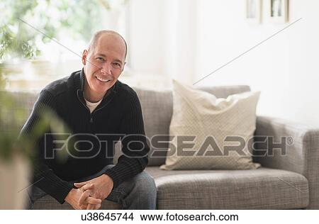 Picture - Portrait of smiling mature man relaxing on sofa in living room . Fotosearch