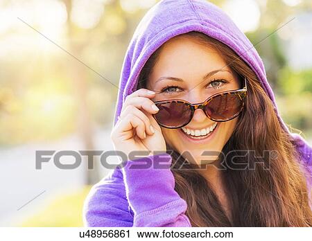 Stock Image - Portrait of smiling woman in hoodie with sunglasses. Fotosearch